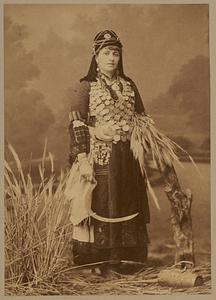 Studio portrait of woman holding scythe and bundle of wheat