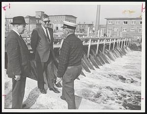 Taunton Crisis is discussed beside flood waters by top officials in that city, Police Chief John A. Bobola, Mayor Benjamin A. Friedman and Fire Chief Carlton W. Gilligan, from left. Mill Dam is in background.
