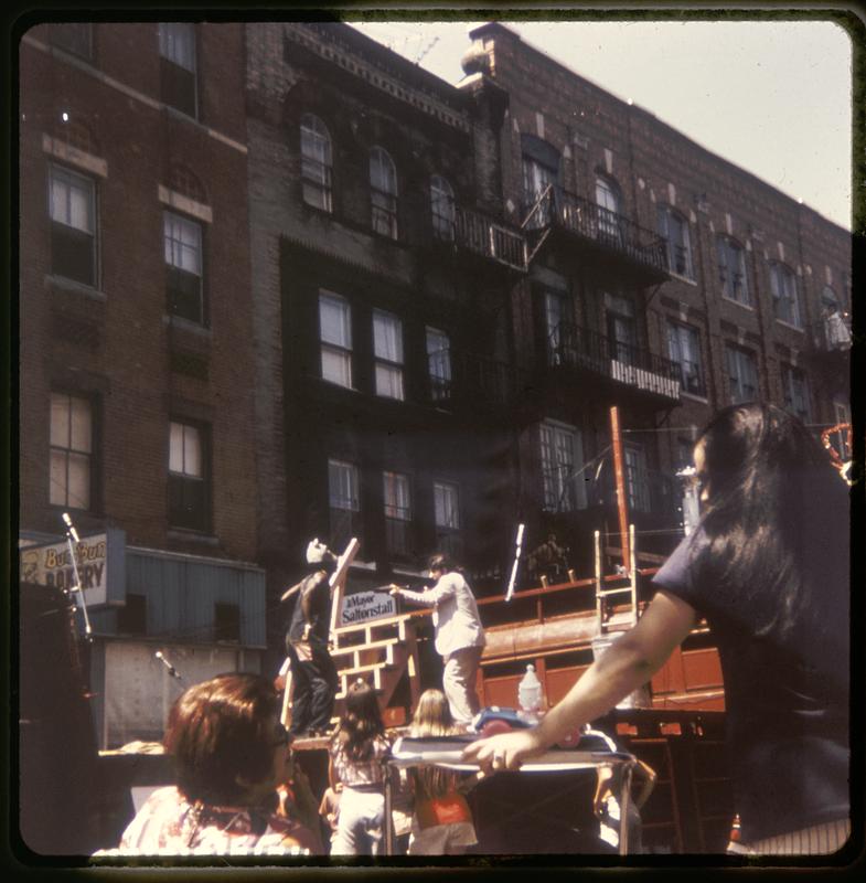 An audience watching a man pointing a rifle at another man during a performance on an outdoor stage