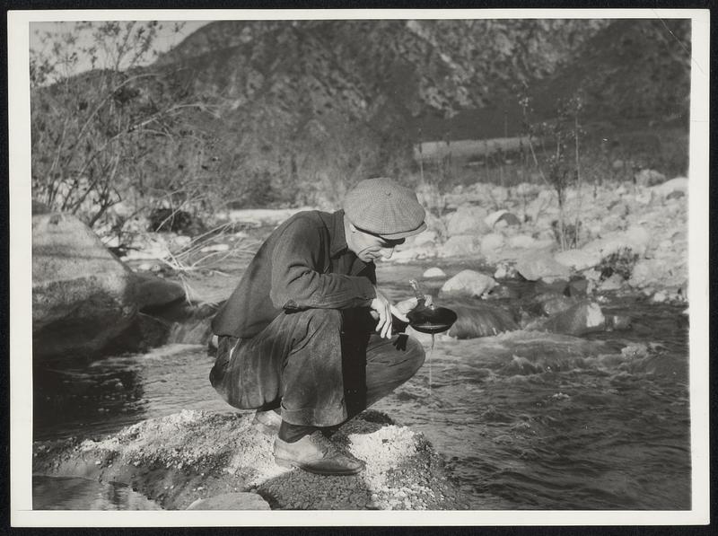 Gold Mining Revives in California. Business Depression has resulted in hundreds of persons at various occupations trying their luck at gold mining in California. This photo, taken near big Tujunga Creek, Less than 30 miles from Los Angeles, shows Fred Livingston, formerly a mewspaper printer in Montana, now unemployed, panning with an ordinary skillet. He and other amateurs say they can make between $2 and $3 a day if they work hard enough.