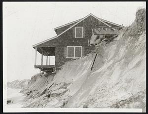 Cape Cod Cottage on Sea street, Dennis, hangs precariously over the washed out bluff. The storm chewed away long stretches of the bluff on Cape Cod Bay. The debris at upper right was a flight of steps which led from the bluff down to the beach.