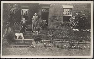 Man, woman, and dog standing in a garden in front of a building