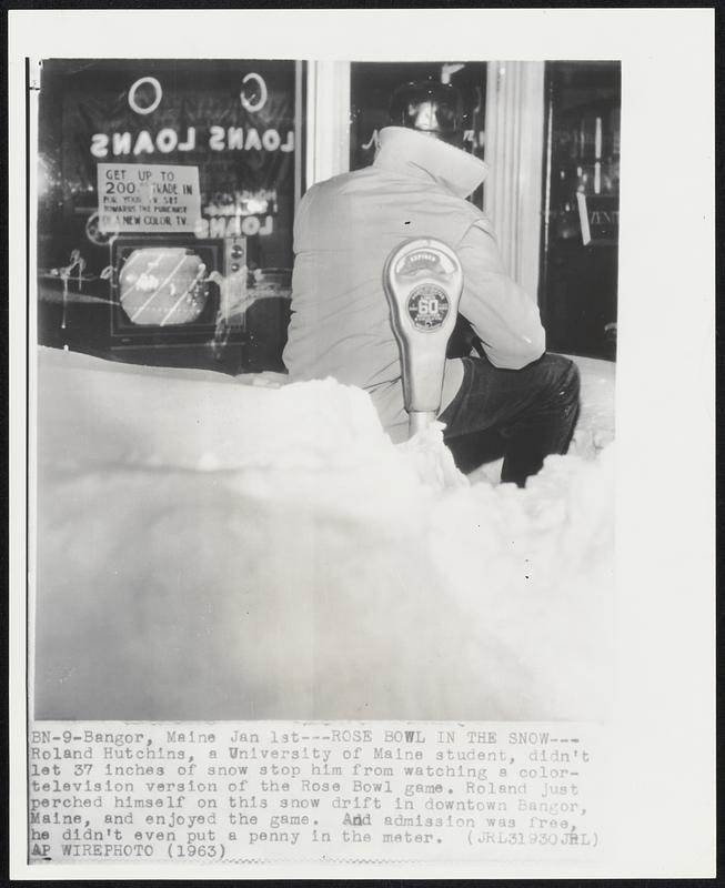 Bangor, Maine. - Rose Bowl In The Snow - Roland Hutchins, a University of Maine student, didn't let 37 inches of snow stop him from watching a color-television version of the Rose Bowl game. Roland just perched himself on this snow drift in downtown Bangor, Maine, and enjoyed the game. And admission was free, he didn't even put a penny in the meter.