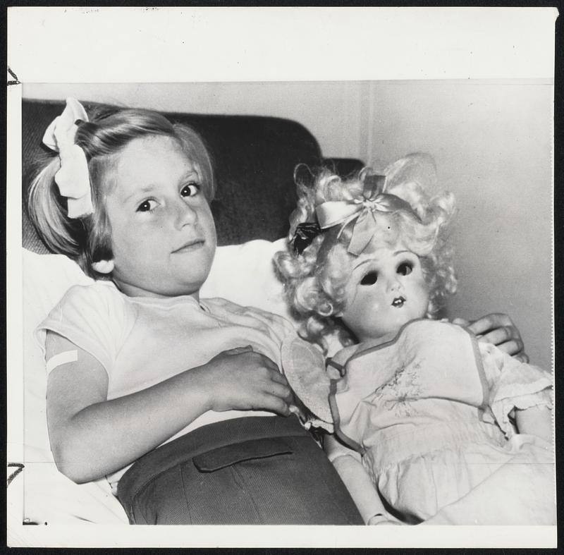 Enroute to Chicago-Janice Dawe, five-year-old English polio victim, holds her doll, Annabelle, as she lies in her bunk on the America in New York after her arrival from England with her parents enroute to Chicago for treatment. Her parents, Mr. and Mrs. Kenneth Dawe, sold their home at Southampton, England, in order to make the trip possible. The child will be treated at the Micheal Reese hospital in Chicago, and the parents are planning to make their home in the U.S.