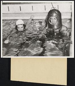 Uses Novel Method to Teach Swimming. Detroit, Mich. -- Ben York, swimming instructor here about to give Ilma Mae Johnston a swimming lesson, utilizes a diving helmet equipped with a microphone to coach his pupils. The instructor is thus able to watch the movements of his pupil, who in turn can listen to criticism and corrections from a loudspeaker.