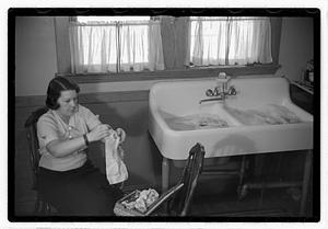 A woman sewing next to a sink full of laundry