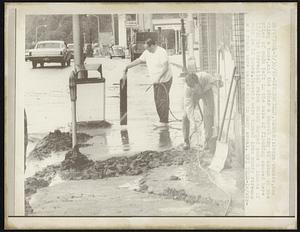 Store owners, one using a hose, and the other a shovel try to clean up the piles of muds left in the wake of flooding caused here (7/29) by torrential rains which dumped some 6 inches of rain in 12 hours. Streets were turned into muddy streams and roads were washed out in many areas.