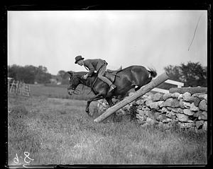 Horse and rider jumping over a low stone wall