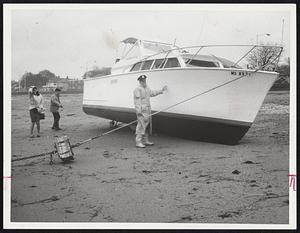Officer Arnold Lamoine of the Metropolitan District Commission Police stands beside a 27-foot cabin cruiser "Sunshine," which dragged its mooring Thursday and skittered over Wollaston Beach.