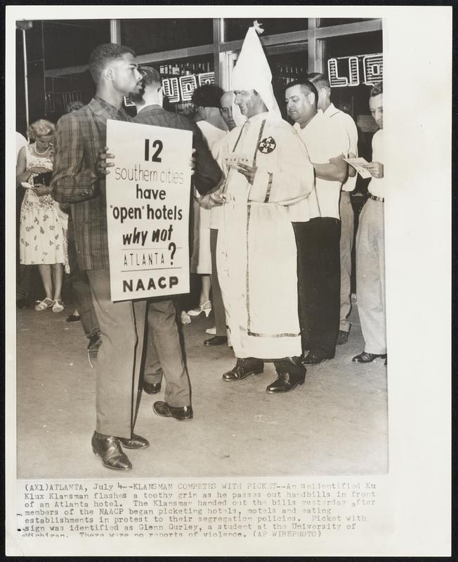 Klansman Competes with Picket--An unidentified Ku Klux Klansman flashes a toothy grin as he passes out handbills in front of an Atlanta hotel. The Klansman handed out the bills yesterday after members of the NAACP began picketing hotels, motels and eating establishments in protest to their segregation policies. Picket with sign was identified as Glenn Gurley, a student at the University of Michigan. There were no reports of violence.