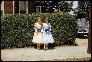 Two girls standing in front of hedge