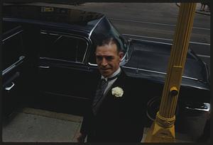 Man with boutonniere standing on sidewalk by car, Jamaica Plain, Massachusetts