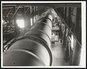 A Vital Wartime Metal - Trouble for the axis is cooking in 270-foot oven at the Anaconda Copper Mining Company's reduction plant here. Largest in the world and the only oven of its kind in the United States, it was put into operation nine months ago at the request of the government, to meet war needs. Its 2,000,000 cubic feet of natural gas used daily would bake many a biscuit. Put to war use, it turns out 300 tons daily of manganese oxide nodules, necessary in the production of armor plate and other shock resistant steels. Manganese oxide is not much to look at, in dull black nodules the size of a small marble, but it is very essential to the steel-maker. As the manganese comes from the Emma mine in Butte, Montana, only present source of manganese carbonate in the country, it appears in shades of pink, ranging from pale rose to deep coral shipped to the reduction plant at Anaconda, it is crushed and milled until almost as fine as flour, then, by "flotation," that mysterious process in which bubbles are used to separate valuable metal ores from useless rock, the lead and zinc are first removed. Another flotation, using soap bubbles, lifts out the manganese carbonate. Pumped to "slurry tanks," some of the moisture is removed by settling and the slurry, containing 30 percent water, goes to the rotary kiln, dried and roasted, it loses its carbon dioxide and forms nodules of the oxide. Dull black in color, now, it is ready for open hearth steel production. The uninterrupted flow of the metal assures plenty of trouble for Herr Hitler and his pals. Here is that great oven which is cooking up trouble for the Axis. Into one end of the huge rotary kiln/goes finely ground manganese carbonate. Roasted, the metal comes out at the far end in the form of nodules of manganese oxide ready for use in the production of open hearth steel.