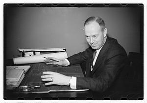 A man seated at a desk, blueprints in front of him