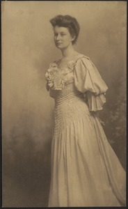 Woman in light shirred dress, standing with arms pulled behind