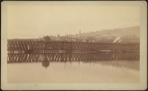 Railroad bridge on water; city in distance