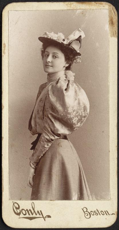 Portrait of fashionably dressed young woman in hat with flowers and ribbon