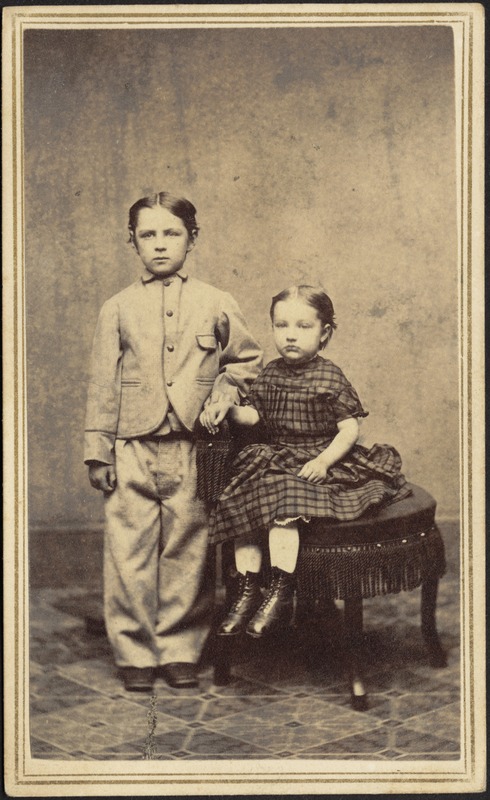 Portrait of young boy standing and seated girl in plaid dress
