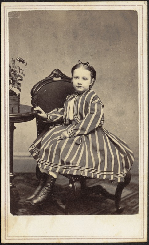 Young girl in striped dress seated in chair, hand on table - Digital ...