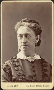 Woman in dark dress with lace collar, braid upon head, long earrings, brooch