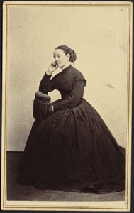 Woman in dark dress seated on chair with fringe