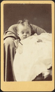 Infant in white frock leaning back in chair