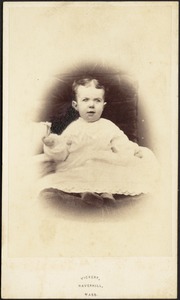 Young child in white frock, seated on dark chair