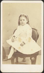 Young girl in white dress and bow seated on chair