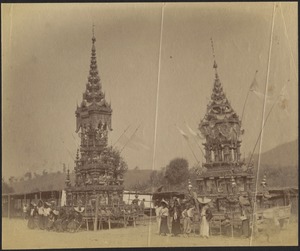 View of rural village; men and women gathered in front of two ornately painted wooden pagoda temples