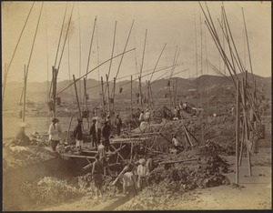 Construction site with several men (some in turbans) standing on scaffolding above trenches; mountains in distance