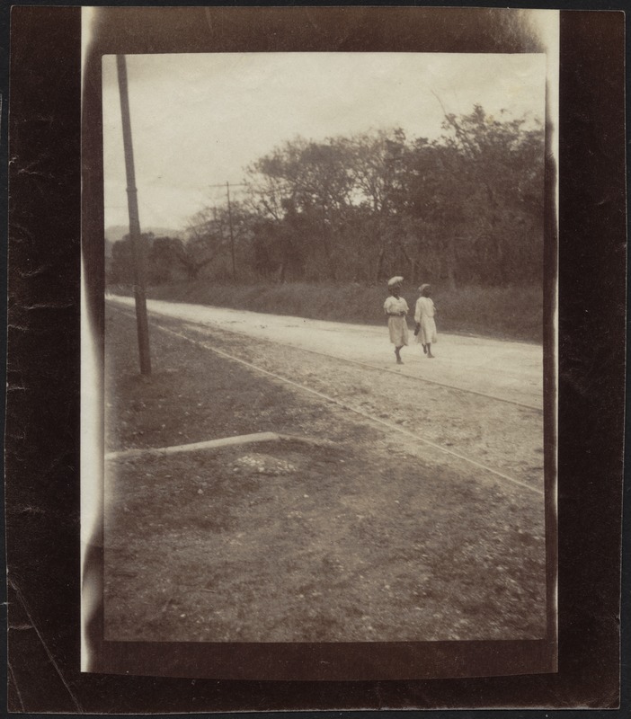 Two women walking down road, one carrying bundle on head