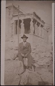 A man wearing a hat and a suit sits in front of the Caryatid porch of the Erechtheion, Athens