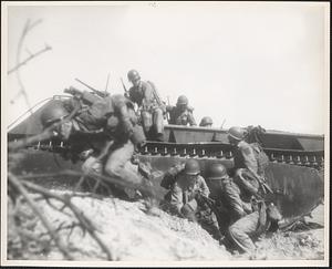 Marines in this wave leap from their amphibious tractor for the shelter of the sand dunes