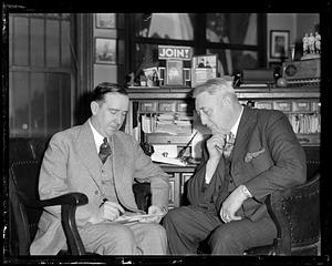 Two seated men looking over paper