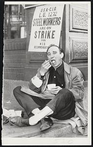 Home Cooking on Picket Line--Steel Worker F.J. Belmont, on picket duty at the Jones and Laughlin Steel corporation plant where he's employed, leans against a corner of the plant building and eats a snack which he carried with him in a lunch pail. Pickets continued on duty as they waited next step in the steel dispute.
