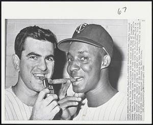Double Congratulations -- Camilo Pascual (left), Minnesota Twins pitcher, lights his own cigar and that of teammate Lenny Green in dressing room tonight as they celebrate birth of baby girls today. Camilo's wife had an 8-pound 14 ounce baby in St. Paul, Minn. This is their second child. Neither of the babies has been named. Pascual is scheduled to pitch tonight against Chicago in Twin Cities.
