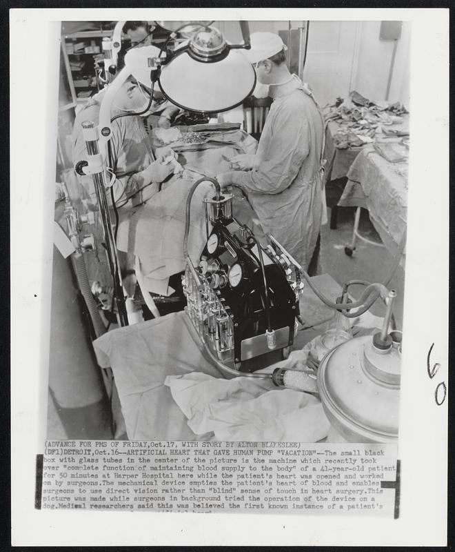 Artificial Heart That Gave Human Pump "Vacation"--The small black box with glass tubes in the center of the picture is the machine which recently took over "complete function of maintaining blood supply to the body" of a 41-year-old patient for 50 minutes at Harper Hospital here while the patient's heart was opened and worked on by surgeons. The mechanical device empties the patient's heart of blood and enables surgeons to use direct vision rather than "blind" sense of touch in heart surgery. This picture was made while surgeons in background tried the operation of the device on a dog. Medical researchers said this was believed the first known instance of a patient's