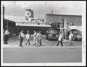 Pickets walk in front of the Texaco plant on Marginal St. in Chelsea today as the shipping strike continues. Trucks are being loaded with gas today and allowed to pass through picket lines. In background is the tanker Texaco Florida.