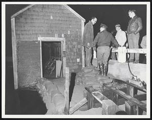 Four men converse, two standing on sandbags