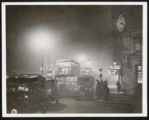 London Blackout?- No, London Fog! Thick fog descended upon busy London town one afternoon recently, casting darkness upon the metropolis long before the usual time. Shown above is Ludgate Circus, with traffic crawling through the murky atmosphere. Pedestrians look like ghosts as they wend their way through the fog. The clock (upper right) shows that the time is 3:20 P.M.