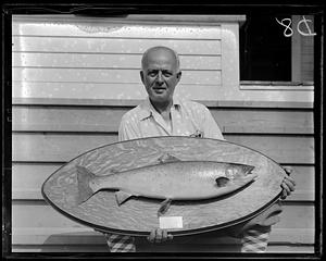 A man holding a fish mounted on an oval wood plaque