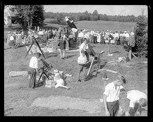 A group of people watching telescopes and cameras being set up outside, possibly to photograph an eclipse