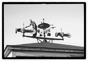 A man adjusting an elaborate device on roof, possibly a weather vane