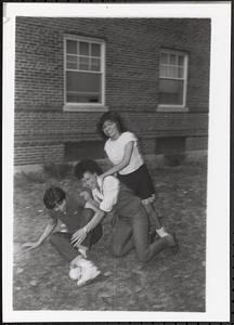 A women and two young people falling on the grass and laughing