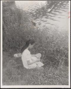 Young woman sitting in grass by the water