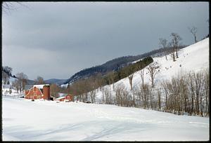 Farm buildings in landscape with snow-covered hills