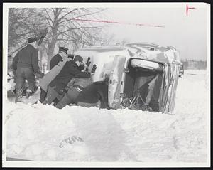 Skidding Accidents were frequent as a result of the season's biggest storm. At left, volunteers and MDC policeman work to right overturned car at Columbia, Circle, Dorchester. At right, lone pedestrian walks past buried cars on narrow, snow clogged Pinckney St. on Beacon Hill.