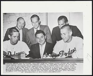 Dodgers ‘Gold Dust Twins’-A teenage brother pitcher and catcher, Joseph Moeller (left), 17, and Gary Moeller (right), 19, sign bonus contracts at Los Angeles today with the Los Angeles Dodger organization. Joe, a pitcher with a high school earned run average of 0.44, and Gary, 1 .480 high school hitter as a catcher, got bonuses totalling an estimated $75,000. Joe will be assigned to the Dodgers’ Spokane, Wash., farm and Gary will go to Kokomo, Ind. Between them is Dodgers Director of Scouting Al Campanis. Rear, left to right: Scout Jack Warner, Joe Moeller Sr., the boys’ father, and scout Lefty Phillips.