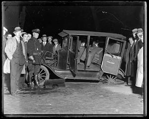 People including police officers stand around a damaged car