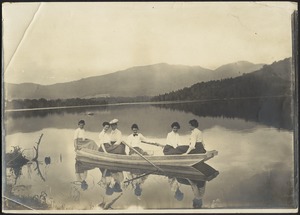 Six women in row boat on lake; mountains in distance